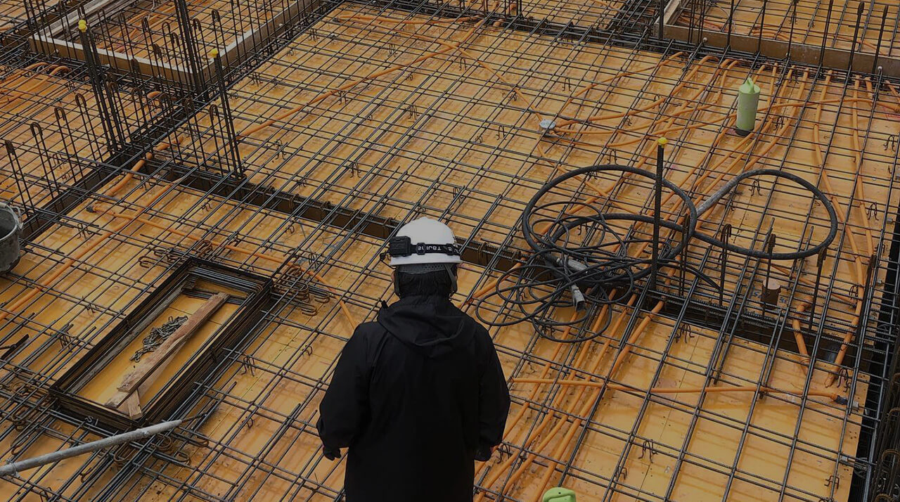 建設現場で鉄筋の組み立て状況を確認する作業員の後ろ姿