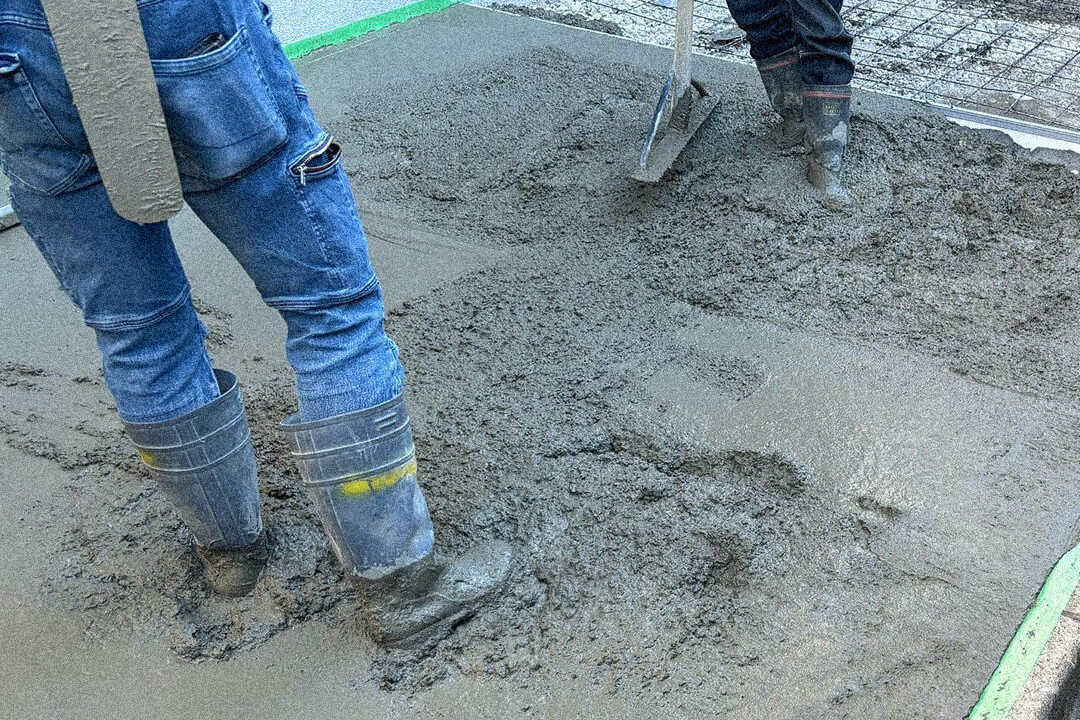 コンクリートを流し込んだ床の上で長靴を履いた作業員が踏み固め、均している様子