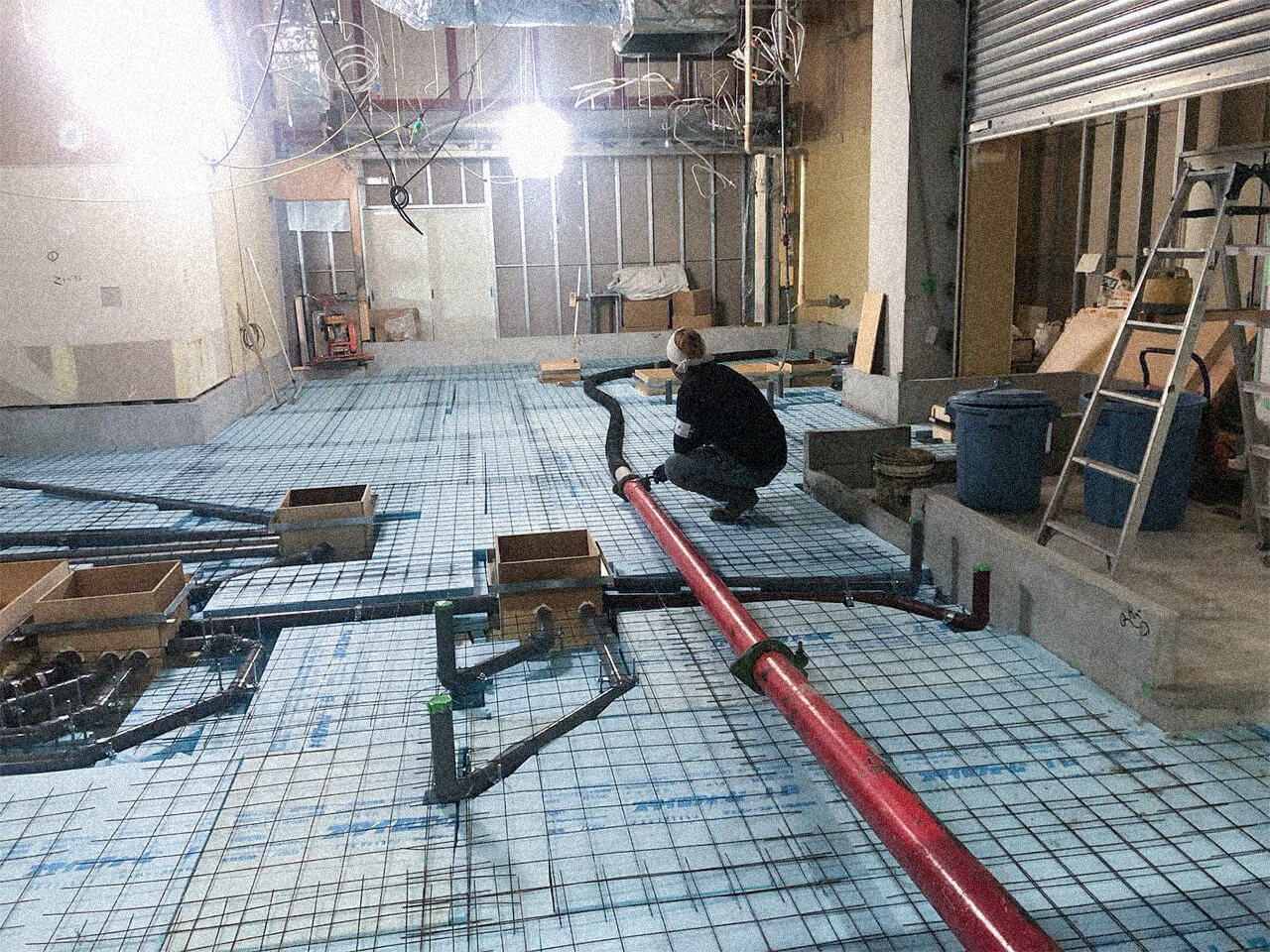 屋内の床工事現場で鉄筋や配管の施工を確認する作業員